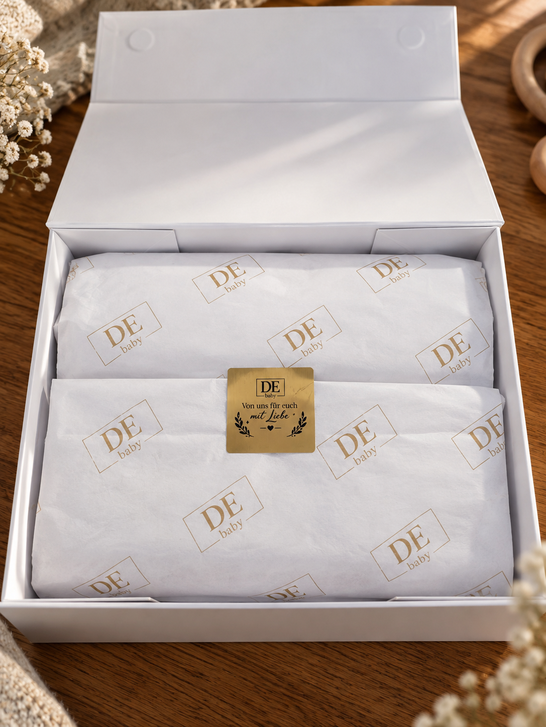 Geöffnete DE Baby Geschenkbox mit weißem Seidenpapier und goldener Markenverpackung
